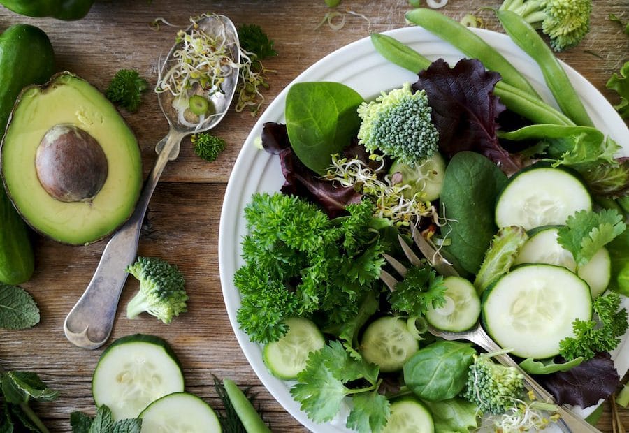 sliced broccoli and cucumber on plate with gray stainless steel fork near green bell pepper, snowpea, and avocado fruit